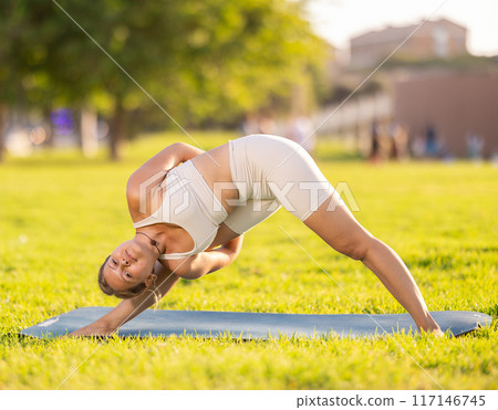 Girl in park on green grass of lawn performs Parshvottanasana Girl in park on green grass of lawn performs Parshvottanasana 117146745