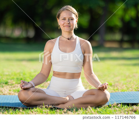 Girl meditating in lotus position during yoga session in summer park Girl meditating in lotus position during yoga session in summer park 117146766