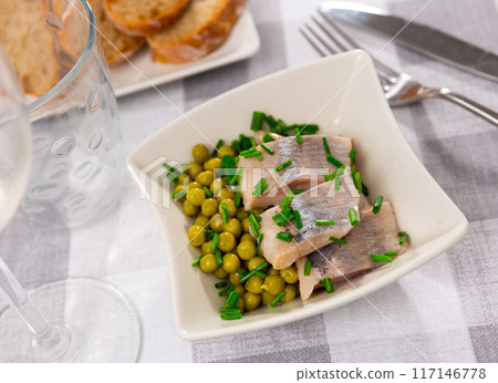 Pieces of salted herring served on plate with green peas 117146778