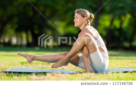 Sporty girl doing arm balancing Elephant Trunk Pose in summer park Sporty girl doing arm balancing Elephant Trunk Pose in summer park 117146786