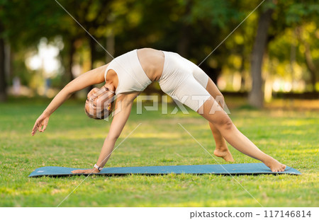 Girl in park on green grass of lawn performs Chamatkarasana Girl in park on green grass of lawn performs Chamatkarasana 117146814