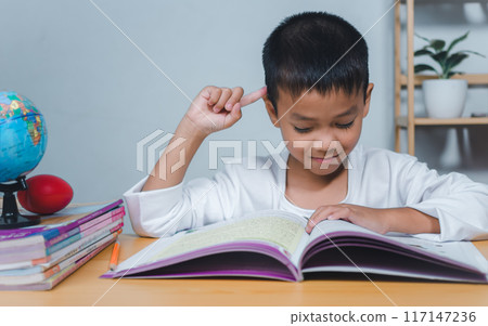 The child smile thinking sitting at table with book. Education, Childhood, People, Homework and school concept. Student learning study reading book while sitting at home. The child smile thinking sitting at table with book. Education, Childhood, People, Homework and school concept. Student learning study reading book while sitting at home. 117147236