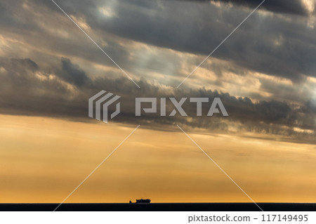 A dramatic ocean sunset with a lone ship and cloudy sky, creating a serene atmosphere A dramatic ocean sunset with a lone ship and cloudy sky, creating a serene atmosphere 117149495