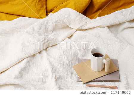 Cozy bed with yellow pillows, notebook, pen and coffee mug. Cozy bed with yellow pillows, notebook, pen and coffee mug. 117149662
