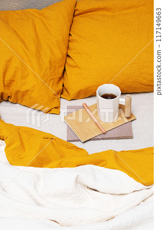 Cozy bed with yellow pillows, notebook, pen and coffee mug. Cozy bed with yellow pillows, notebook, pen and coffee mug. 117149663