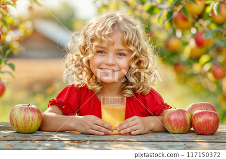 Cute child with apples and juice glass. Kid girl in red dress with fruit harvest. Baby in autumn orchard. Food farm garden with tree. Family apple pick banner. Happy little child in summer countryside 117150372