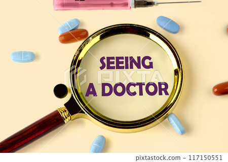 Medicine concept. The inscription SEEING A DOCTOR through a magnifying glass on a yellow background with scattered pills Medicine concept. The inscription SEEING A DOCTOR through a magnifying glass on a yellow background with scattered pills 117150551