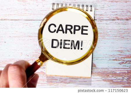 Carpe Diem Phrase It means Seize the moment in a white notebook on old boards through a magnifying glass in a man's hand Carpe Diem Phrase It means Seize the moment in a white notebook on old boards through a magnifying glass in a man's hand 117150623