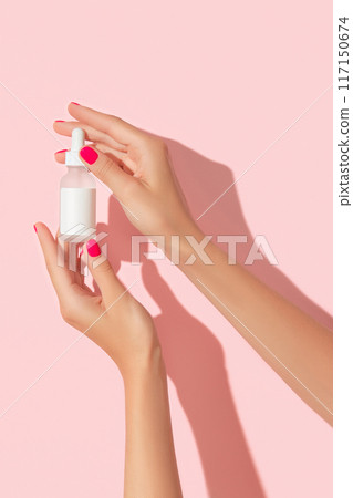 Womans hands holding dropper serum on pastel pink background. Self care beauty treatment concept Womans hands holding dropper serum on pastel pink background. Self care beauty treatment concept 117150674