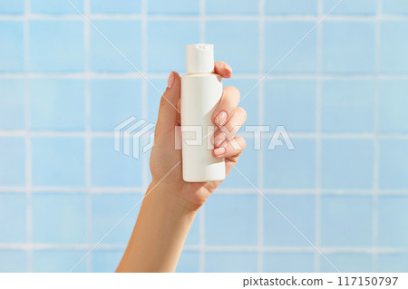 Womans hand holding white tube on blue tile background. Beauty treatment. Skin care routine Womans hand holding white tube on blue tile background. Beauty treatment. Skin care routine 117150797