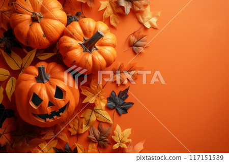 Spooky Halloween setup with carved pumpkins and autumn leaves on an orange backdrop 117151589