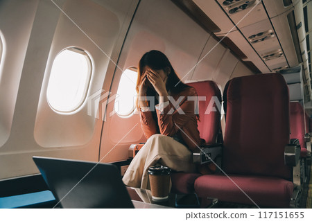 Photo of a frustrated woman sitting on an airplane with her head in her hands. Asian woman sitting in a seat in airplane 117151655