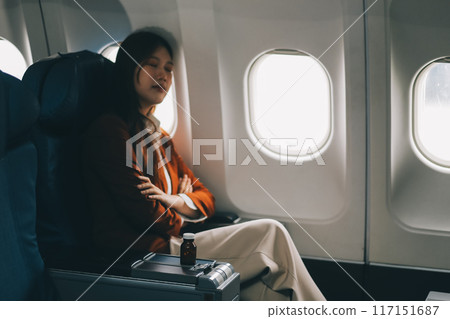 Photo of a frustrated woman sitting on an airplane with her head in her hands. Asian woman sitting in a seat in airplane 117151687