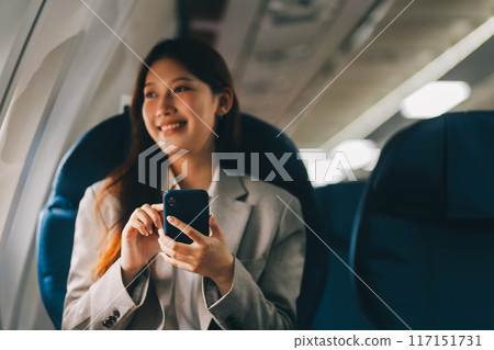 Asian woman sitting in a seat in airplane and looking out the window going on a trip vacation travel concept.Capture the allure of wanderlust with this stunning image 117151731