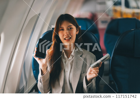 A young Asian woman, seated as an airplane passenger, contemplates dollar bills, reflecting on lucrative opportunities and aspirations towards billionaire status. A young Asian woman, seated as an airplane passenger, contemplates dollar bills, reflecting on lucrative opportunities and aspirations towards billionaire status. 117151742