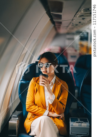 A young Asian woman, seated as an airplane passenger, contemplates dollar bills, reflecting on lucrative opportunities and aspirations towards billionaire status. A young Asian woman, seated as an airplane passenger, contemplates dollar bills, reflecting on lucrative opportunities and aspirations towards billionaire status. 117151746