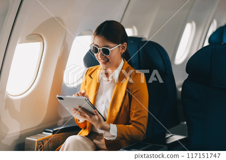 A young Asian woman, seated as an airplane passenger, contemplates dollar bills, reflecting on lucrative opportunities and aspirations towards billionaire status. A young Asian woman, seated as an airplane passenger, contemplates dollar bills, reflecting on lucrative opportunities and aspirations towards billionaire status. 117151747