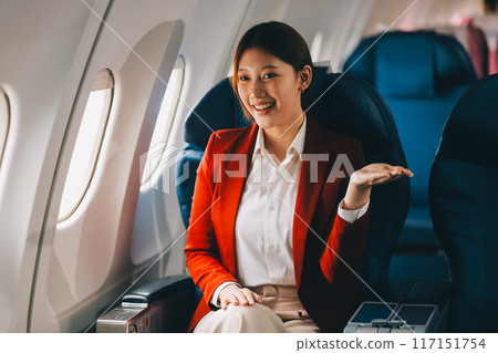 A young Asian woman, seated as an airplane passenger, contemplates dollar bills, reflecting on lucrative opportunities and aspirations towards billionaire status. A young Asian woman, seated as an airplane passenger, contemplates dollar bills, reflecting on lucrative opportunities and aspirations towards billionaire status. 117151754
