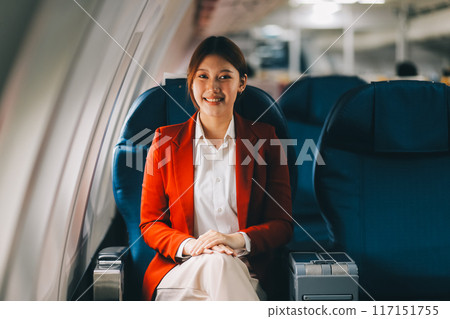 A young Asian woman, seated as an airplane passenger, contemplates dollar bills, reflecting on lucrative opportunities and aspirations towards billionaire status. A young Asian woman, seated as an airplane passenger, contemplates dollar bills, reflecting on lucrative opportunities and aspirations towards billionaire status. 117151755