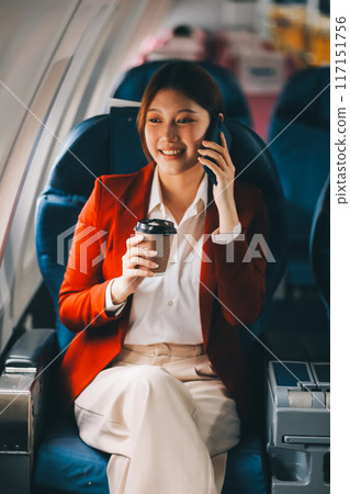 A young Asian woman, seated as an airplane passenger, contemplates dollar bills, reflecting on lucrative opportunities and aspirations towards billionaire status. A young Asian woman, seated as an airplane passenger, contemplates dollar bills, reflecting on lucrative opportunities and aspirations towards billionaire status. 117151756