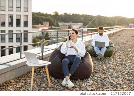 Young professionals working remotely on rooftop with laptops 117152097