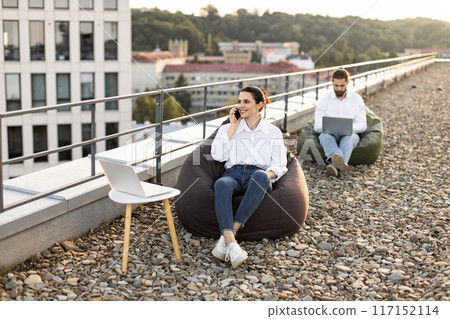 Business professionals working outdoors on rooftop with laptops 117152114
