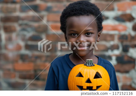 Cheerful boy smiles while holding a carved pumpkin against a brick wall Cheerful boy smiles while holding a carved pumpkin against a brick wall 117152116