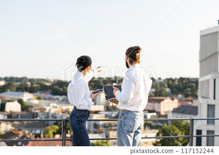 Business colleagues discussing project on rooftop with city view Business colleagues discussing project on rooftop with city view 117152244