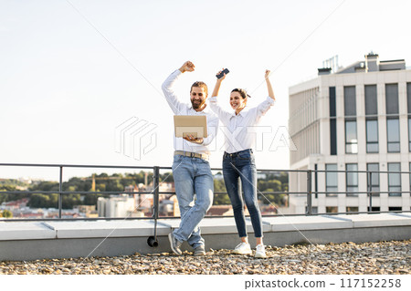 Successful business colleagues celebrating on rooftop with laptop and phone Successful business colleagues celebrating on rooftop with laptop and phone 117152258