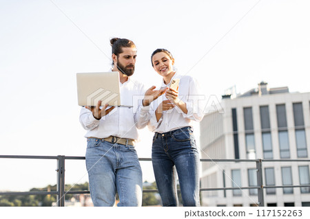 Young professionals collaborating outdoors with laptop and smartphone 117152263