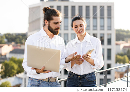 Young professionals collaborating outside with laptop and smartphone Young professionals collaborating outside with laptop and smartphone 117152274