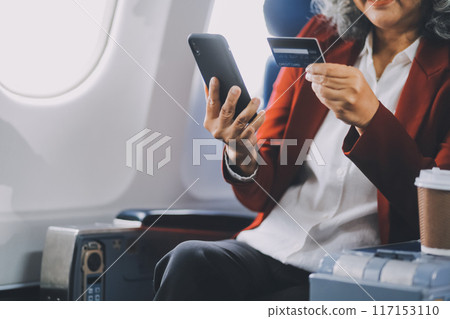 An adult woman sits by the window on a passenger plane, eagerly traveling abroad. She gazes at the clouds, anticipating new experiences and adventures in a foreign land. An adult woman sits by the window on a passenger plane, eagerly traveling abroad. She gazes at the clouds, anticipating new experiences and adventures in a foreign land. 117153110