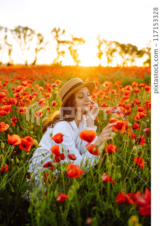 Young girl in hat posing in the poppy field. Portrait of curly girl walking in poppy field at sunset. Summertime. Young girl in hat posing in the poppy field. Portrait of curly girl walking in poppy field at sunset. Summertime. 117153328
