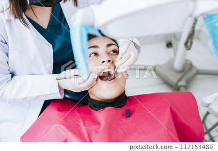 Top view of dentist doing cleaning to female patient lying down. Dentist doctor examining mouth to patient lying on chair, Female dentist examining mouth to patient lying down 117153489