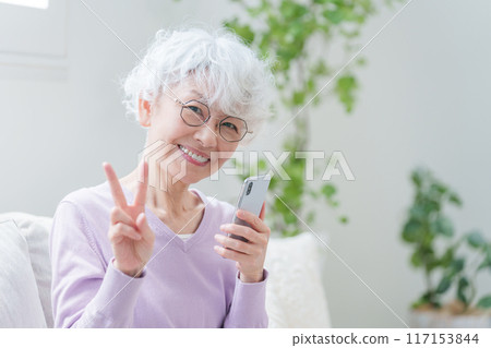 Elderly woman making a peace sign with a smartphone 117153844