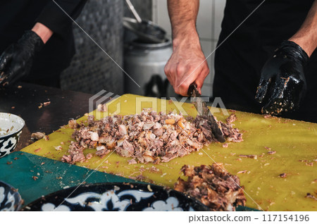 male chefs cut boiled beef meat with knives on a cutting board in the kitchen at Restaurant in Tashkent in Uzbekistan male chefs cut boiled beef meat with knives on a cutting board in the kitchen at Restaurant in Tashkent in Uzbekistan 117154196