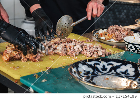 male chefs cut boiled beef meat with knives on a cutting board in kitchen at restaurant in Uzbekistan 117154199