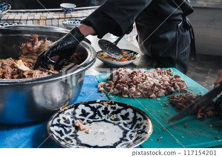 male hands chefs cut boiled beef meat with knives for cooking oriental Uzbek pilaf in kitchen at restaurant in Uzbekistan 117154201