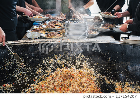 male chefs cook Uzbek rice pilaf with vegetables in cauldron in the kitchen of restaurant. Traditional Asian Uzbek cuisine. Central Asian Pilaf Center in Uzbekistan in Tashkent male chefs cook Uzbek rice pilaf with vegetables in cauldron in the kitchen of restaurant. Traditional Asian Uzbek cuisine. Central Asian Pilaf Center in Uzbekistan in Tashkent 117154207