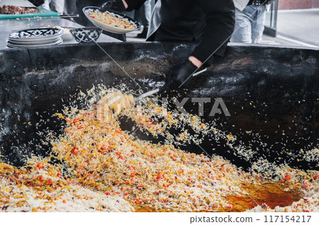 male cook cooked Uzbek pilaf from cauldron on a plate in the kitchen. Traditional Oriental Arabic cuisine. Central Asian Pilaf Center in Uzbekistan in Tashkent male cook cooked Uzbek pilaf from cauldron on a plate in the kitchen. Traditional Oriental Arabic cuisine. Central Asian Pilaf Center in Uzbekistan in Tashkent 117154217