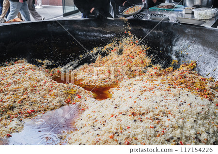 male puts cooked Uzbek pilaf from a large cauldron on a plate in the kitchen. Traditional Oriental Arabic cuisine male puts cooked Uzbek pilaf from a large cauldron on a plate in the kitchen. Traditional Oriental Arabic cuisine 117154226