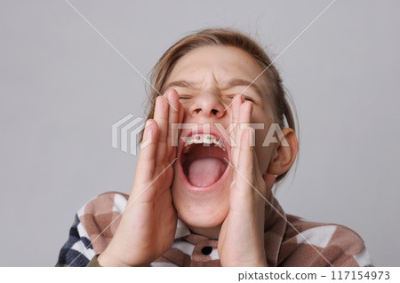close-up portrait of a teenager with braces, the boy screams attracting attention, tell me urgently close-up portrait of a teenager with braces, the boy screams attracting attention, tell me urgently 117154973