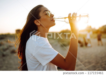 Pretty girl drinking beer at the beach at sunset. Young woman enjoying on beach holiday. Summertime 117155461