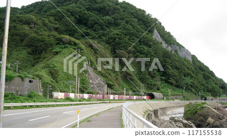 A freight train travelling along the mountainous coast enters a tunnel 117155538