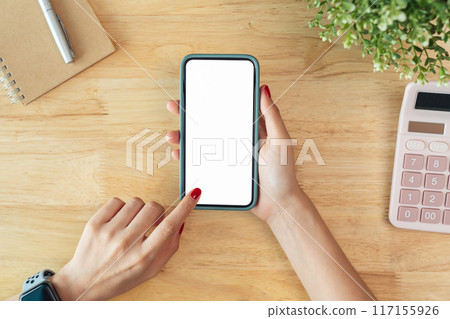 Female hands holding smartphone with mockup of blank screen on desk in office room. 117155926