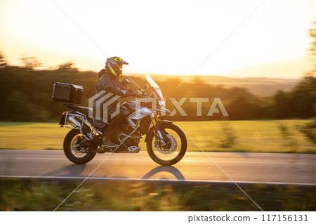 Driver riding motorcycle on empty road during sunset 117156131