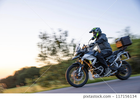 Driver riding motorcycle on empty road during sunset Driver riding motorcycle on empty road during sunset 117156134