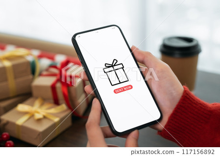 Hand using smartphone with sent gift to mobile application and festive decorations on the black background. 117156892