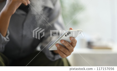 Cropped image of man smoking disposable electronic cigarette and using mobile phone Cropped image of man smoking disposable electronic cigarette and using mobile phone 117157056