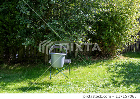 Bucket Hanging On a Metal Chair Back in a Sunlit Urban Garden 117157065